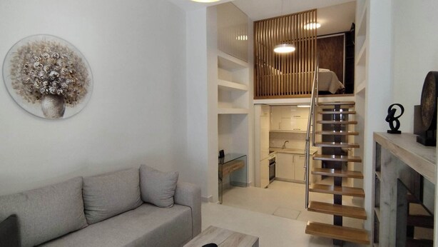 A modern living room with a grey sofa, a wooden staircase, and a kitchen area visible through an open door. - Corfu Luxury Loft2 by Corfuescapes (Corfu)