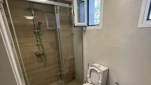 A modern bathroom with a glass-enclosed shower, a toilet, and a small window. - Corfu Luxury Loft2 by Corfuescapes (Corfu)