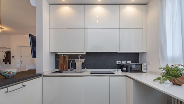 Une cuisine moderne avec des meubles blancs, un plan de travail noir, un four à micro-ondes et un évier.