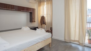 Une chambre d’hôtel moderne avec un lit en bois, une armoire, un miroir, une fenêtre avec des rideaux et une plante en pot près de la fenêtre.