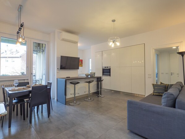 A modern kitchen with a built-in oven, a dining area with a table and chairs, and a living area with a sofa.