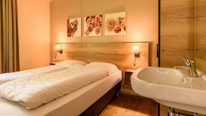 A hotel room with a double bed, a wooden headboard, a wall-mounted sink, and three framed pictures on the wall. - Bungalow in Putten with COPD-Friendly Design (Putten)