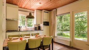 A modern kitchen with white cabinets, a dining table with chairs, and large windows offering a view of greenery. - Bungalow in Putten with COPD-Friendly Design (Putten)