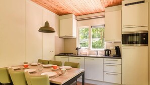 A modern kitchen with white cabinets, a wooden ceiling, and a dining area with green chairs and a table set for four. - Bungalow in Putten with COPD-Friendly Design (Putten)