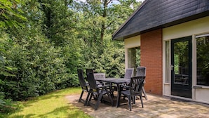 A patio with a table and chairs, surrounded by lush greenery. - Bungalow in Putten with COPD-Friendly Design (Putten)