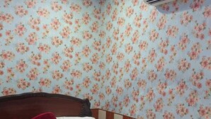 Une chambre avec un papier peint à motifs floraux, un lit avec une tête de lit en bois et un climatiseur fixé au mur.