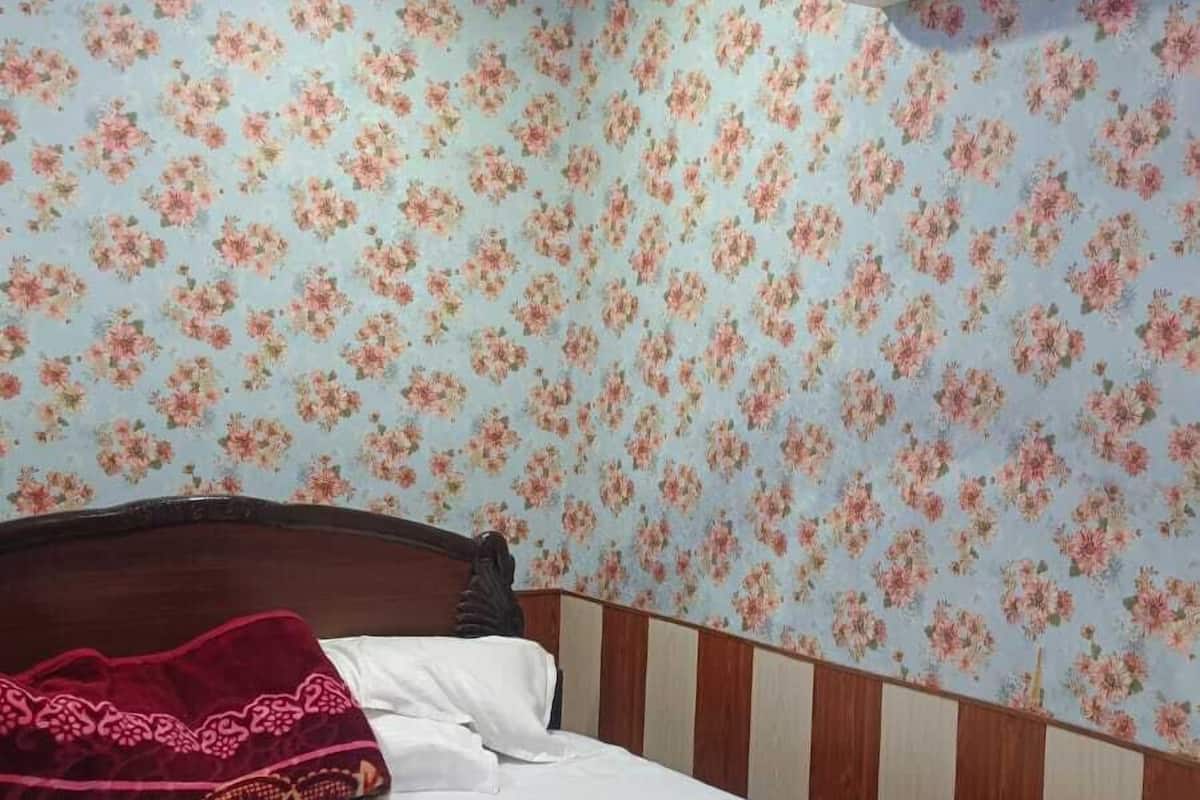 A bedroom with a floral wallpaper, a bed with a wooden headboard, and an air conditioner on the wall.