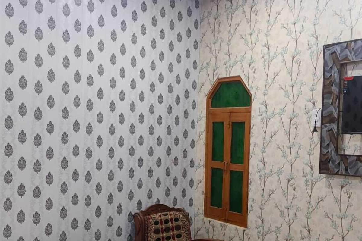 A bedroom with a bed, a chair, a window, and patterned wallpaper.