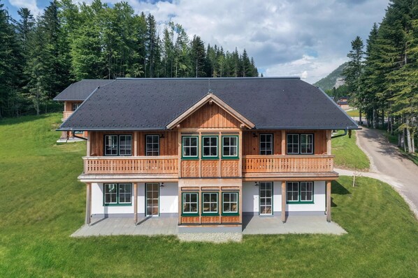 Ein zweistöckiges Holzhaus mit Balkon, umgeben von einer Rasenfläche und Bäumen.