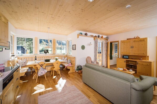 A cozy, well-lit wooden cabin interior with a dining area, sofa, and wooden cabinets.