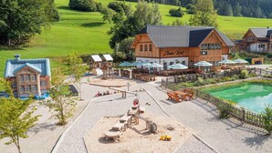 A wooden building with a sign reading "Zoe's Well" and a pool area with tables and umbrellas.