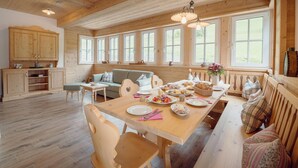 A wooden interior with a dining table set for a meal, a sofa, and a kitchen area with cabinets and a countertop. - Chalet near Lake Grundlsee & Ski Lift (Grundlsee)