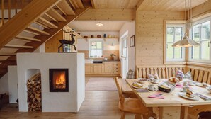 Un intérieur chaleureux, avec des murs en bois et une cheminée, un coin repas où une table est dressée pour le repas, et une cuisine en arrière-plan.