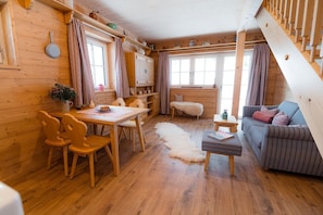 A cozy cabin interior with wooden walls, a dining area with chairs, a sofa, and a staircase.