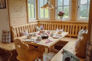 Et spiseområde i træ med bænk og bord, omgivet af vinduer med udsigt til grønne områder.