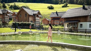 Une maison en bois avec un balcon, un étang et une personne qui passe.