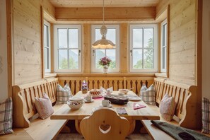 A wooden dining table with benches, a hanging light fixture, and a window with a view of mountains. - Chalet in Grundlsee near Ski Slopes (Grundlsee)