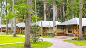 A row of cabins with wooden decks and picnic tables, surrounded by a forested area. - Luxuszelt im Serengeti Park (Hodenhagen)