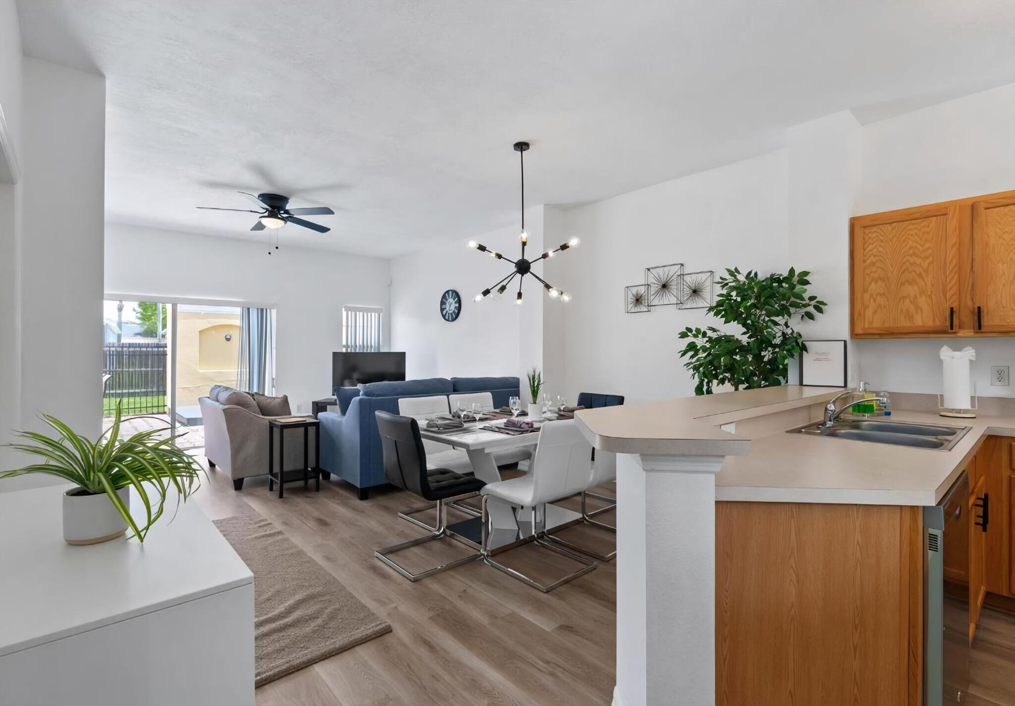Una cocina moderna con una isla central, un área de comedor con mesa y sillas blancas, un sofá azul y un ventilador de techo.