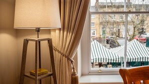 Ein Zimmer mit einer Lampe auf einem Holztisch, einem Fenster mit Vorhängen und Blick auf die Straße.