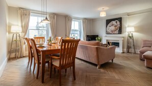 Ein Wohnzimmer mit Esstisch, Stühlen, einer Couch, einem Kamin und einem Fernseher.