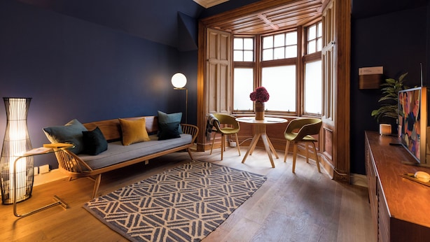 A modern living room with a sofa, chairs, a coffee table, and a large window with wooden shutters. - JOIVY Contemporary Cottage with Parking (Edinburgh)