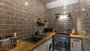 A modern kitchen with grey tiled walls, a wooden countertop, a stainless steel toaster, a microwave, a kettle, and a dishwasher. - JOIVY Contemporary Cottage with Parking (Edinburgh)
