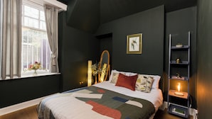 A bedroom with a bed, a window with curtains, a bedside table with a lamp, and a wall-mounted shelf. - JOIVY Contemporary Cottage with Parking (Edinburgh)
