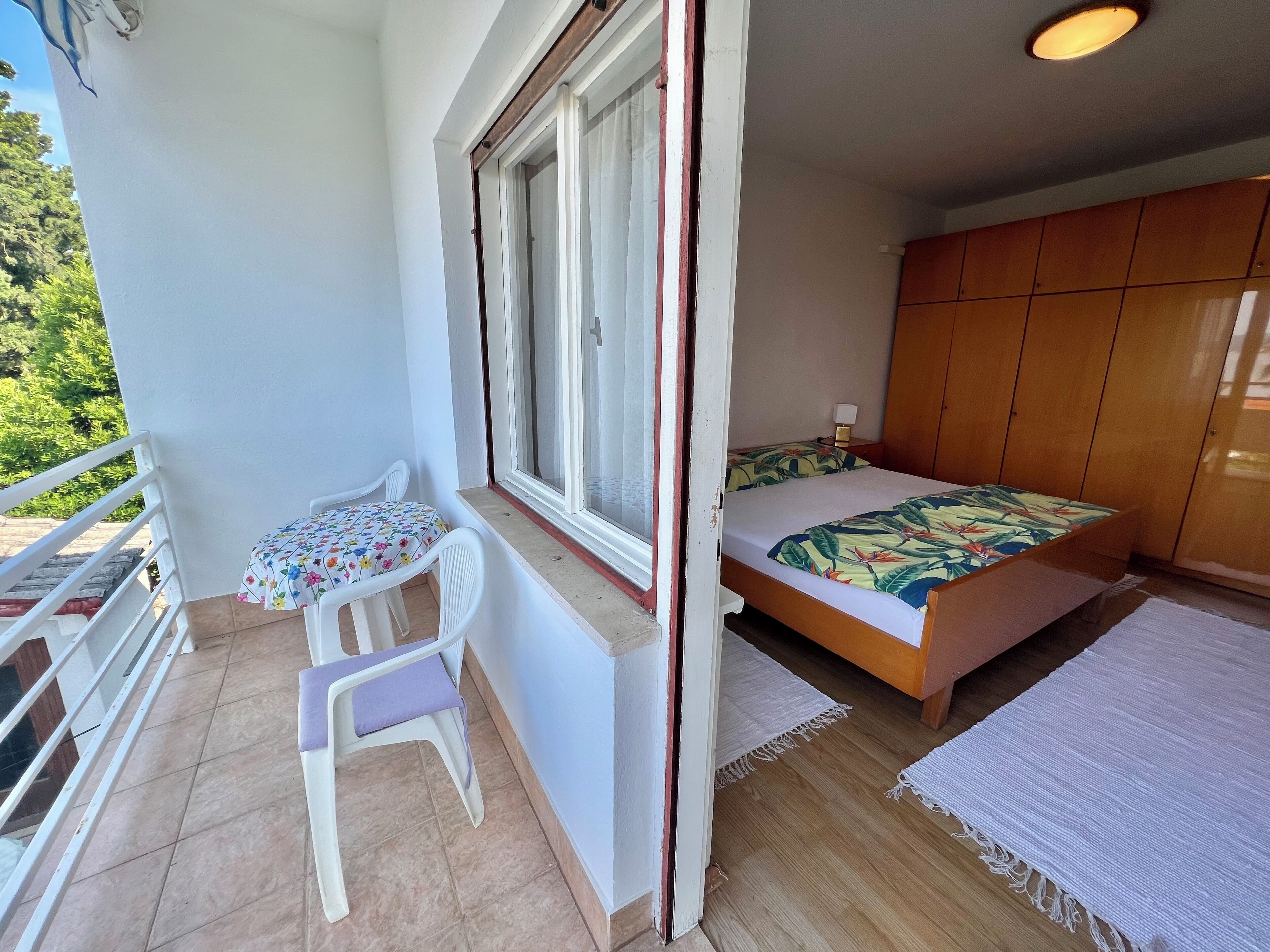 Ein kleines Schlafzimmer mit einem Bett, einem Nachttisch, einem Fenster und einem Balkon mit Stuhl und Tisch.