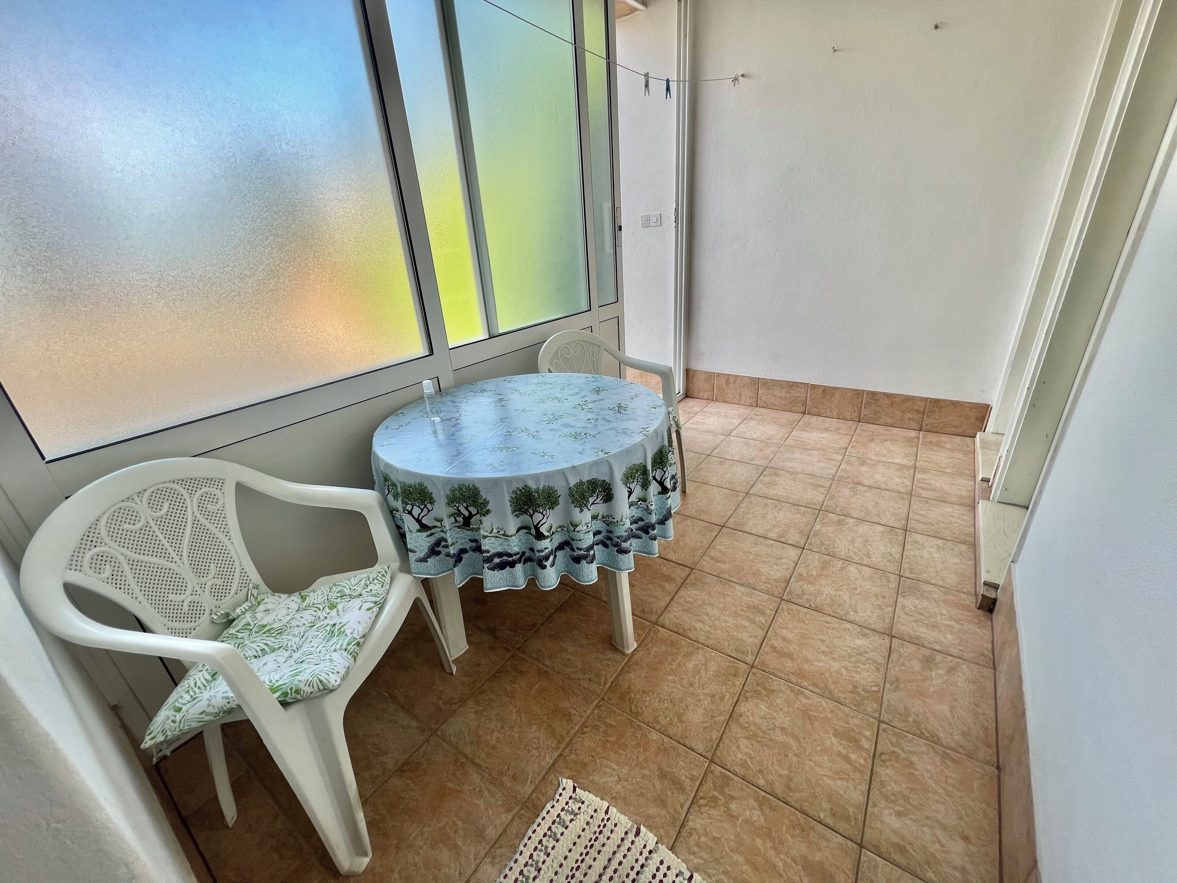 A small balcony with a round table and two chairs, a tiled floor, and a frosted glass door.