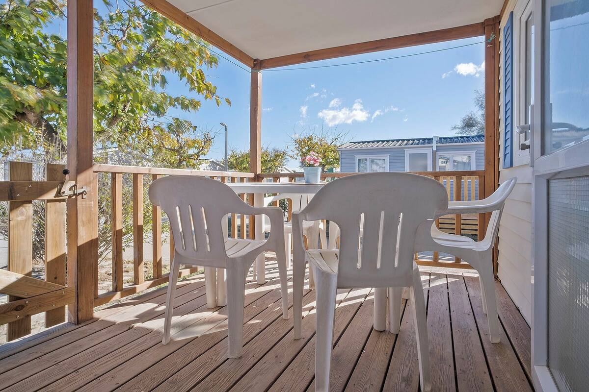 A wooden deck with two white plastic chairs and a table, overlooking a residential area with houses.