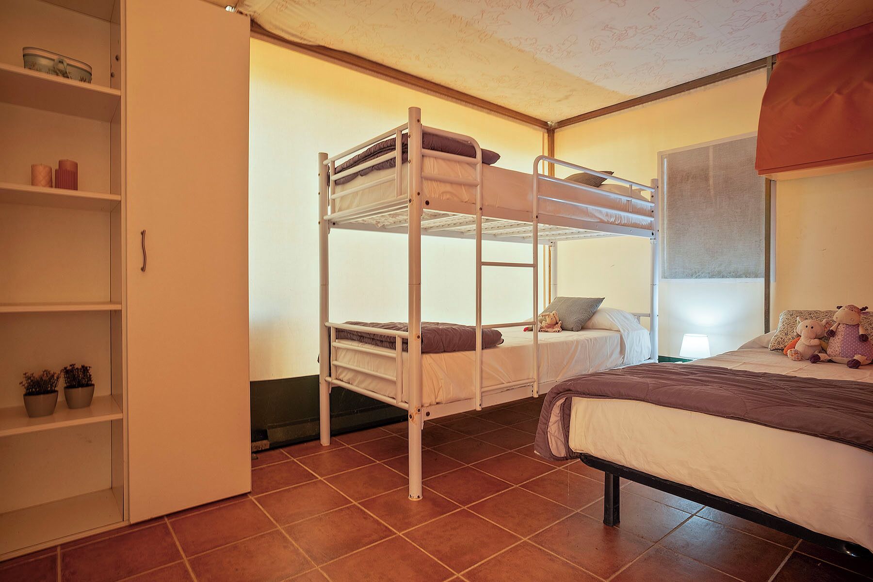 Une chambre de type dortoir avec des lits superposés, un lit, une étagère avec des plantes en pot et une fenêtre donnant sur un paysage agréable.