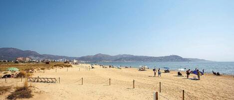 A wide sandy beach with a clear sky and mountains in the background.