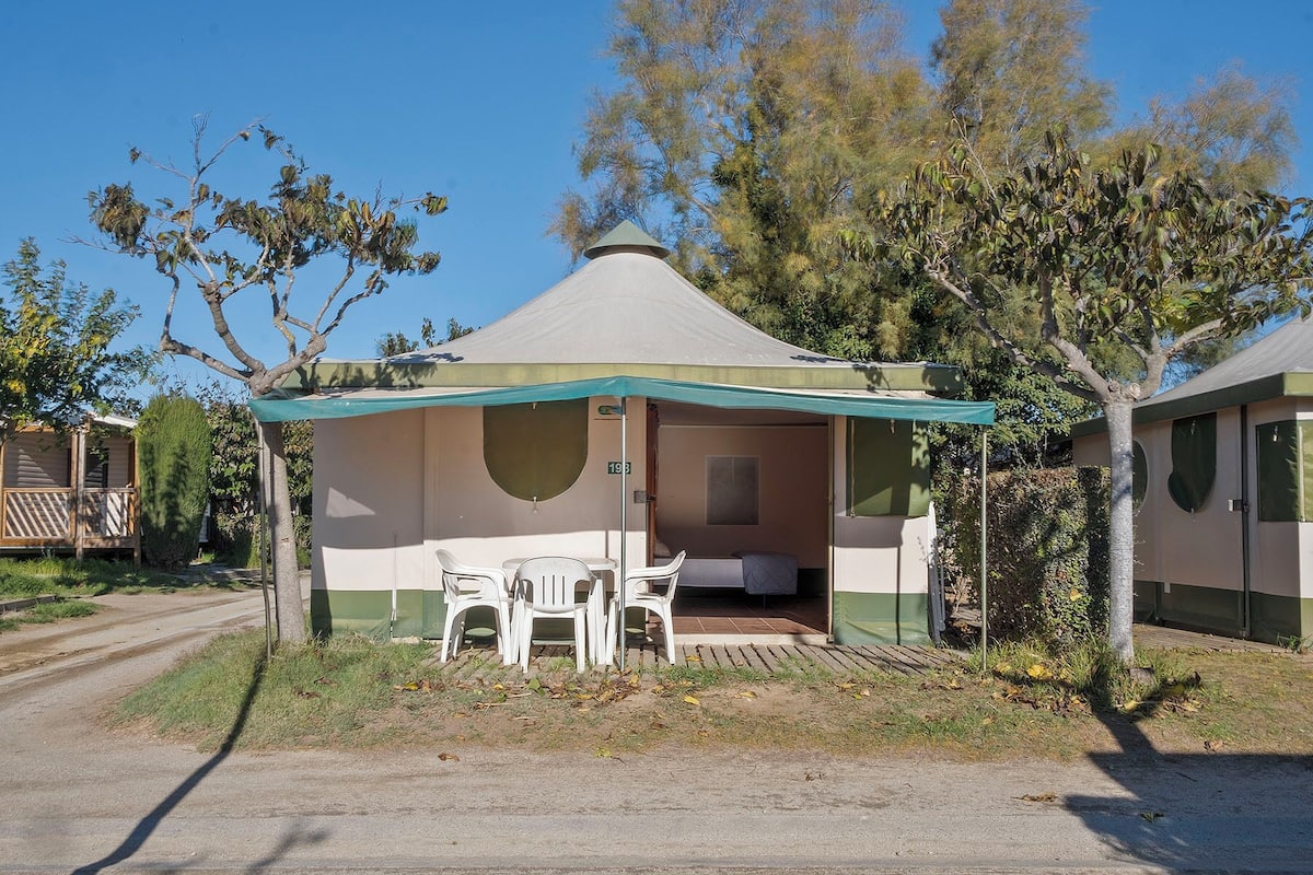A single-room tent with a covered patio area, a small table, and two chairs.