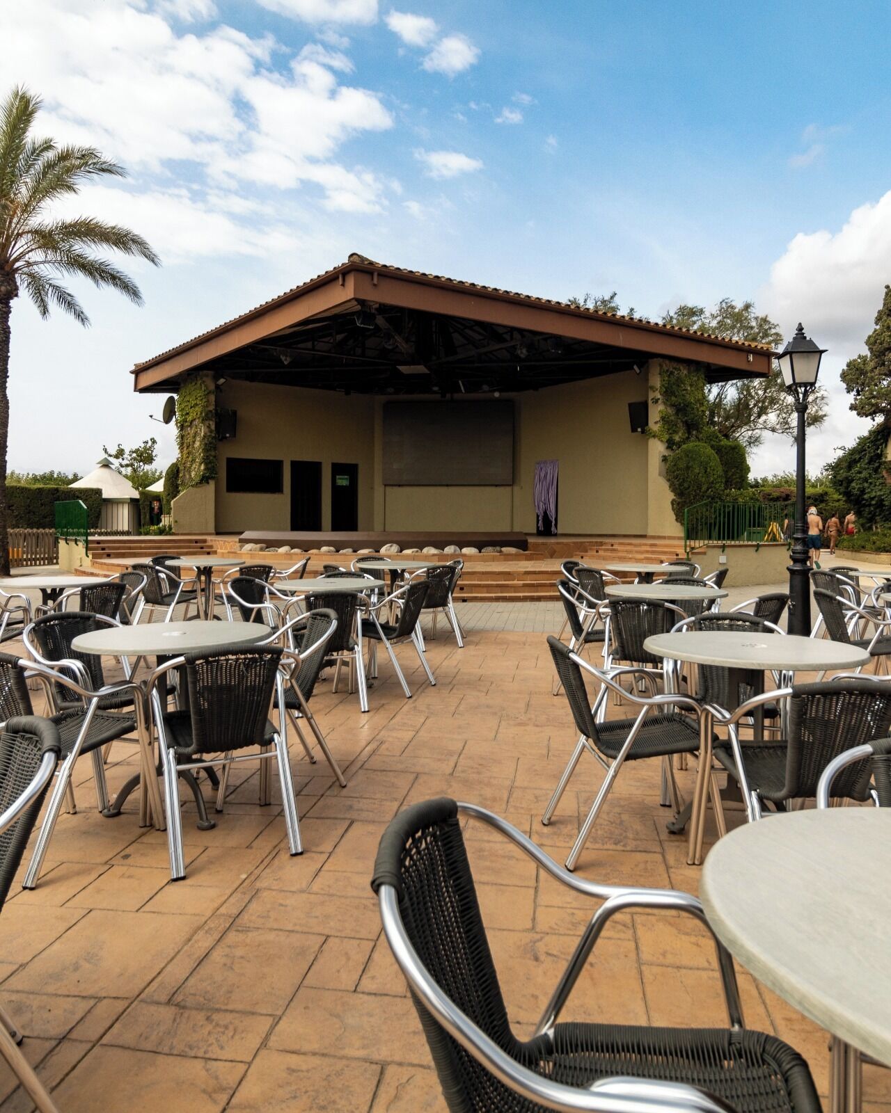 An outdoor patio area with round tables and chairs, a covered stage, and a view of the surrounding landscape.