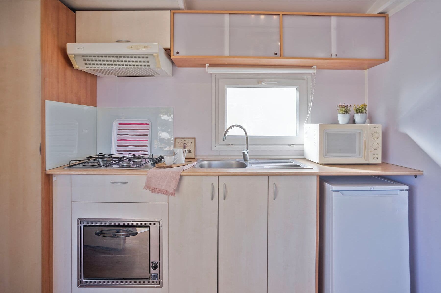 A compact kitchenette with a gas stove, microwave, sink, and a small refrigerator.