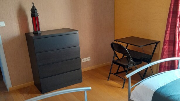 A bedroom with two beds, a small desk, a dresser, and a red curtain. - Le Menhir  (Avrille)