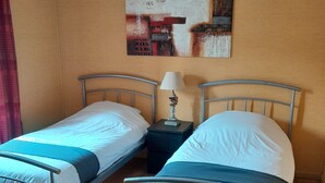 A room with two metal beds, a nightstand with a lamp, and a painting on the wall. - Le Menhir  (Avrille)