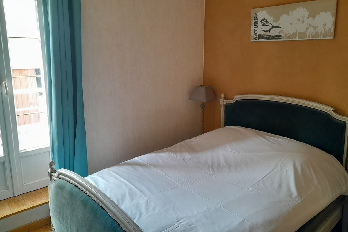 A bedroom with a bed, a window with curtains, a lamp, and a wall decoration.