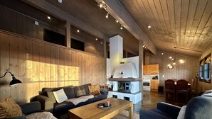 A spacious living area with a wooden ceiling, a fireplace, a dining area, and a kitchen with wooden cabinets.