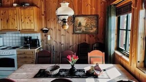 A wooden cabin interior with a kitchen area, a dining table with chairs, and a window with a view.