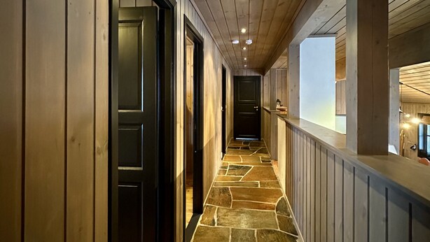 A hallway with wooden walls and a stone floor, leading to a room with a window and a counter.