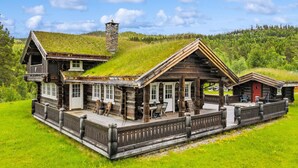 A log cabin with a grassy roof, a stone chimney, and a wooden deck with outdoor seating. - Luxury Cabin at Nesfjellet with sauna, bbq, close to ski & golf (Nesbyen)
