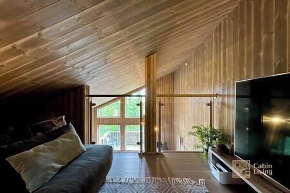 A cabin interior with a wooden ceiling, a large flat-screen TV, a sofa, and a sliding glass door leading outside.