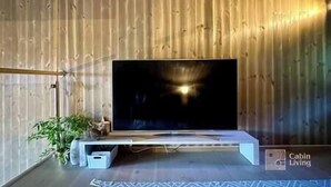 A modern living room with a large flat-screen TV mounted on a wooden wall, a minimalist entertainment unit, and a potted plant. - Sjusjøen ski in/out, ski storage, Wifi, grill & EV-charger, modern apartment! (Sjusjøen)