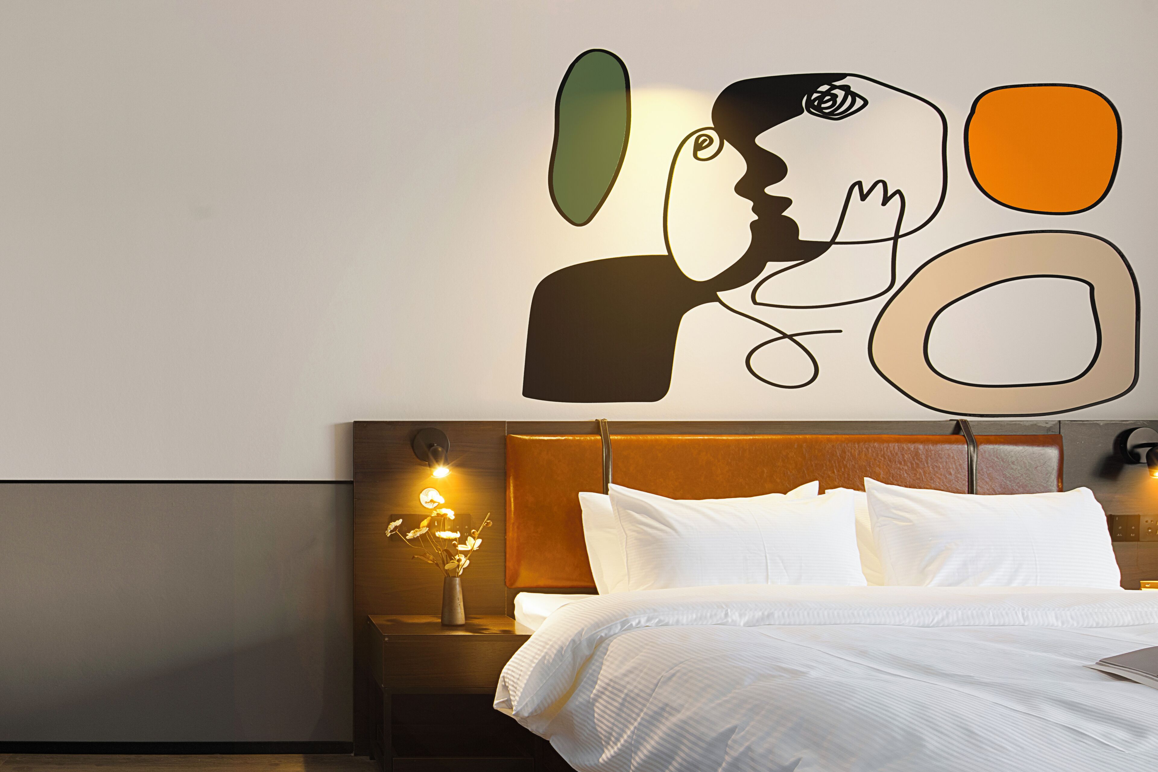 A hotel room with a bed, a nightstand with a lamp, and a wall art piece.