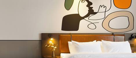 A hotel room with a bed, a nightstand with a lamp, and a wall art piece.