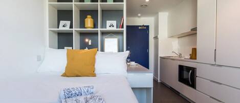 Una habitación de hotel moderna con cama, un escritorio pequeño, kitchenette y armario.