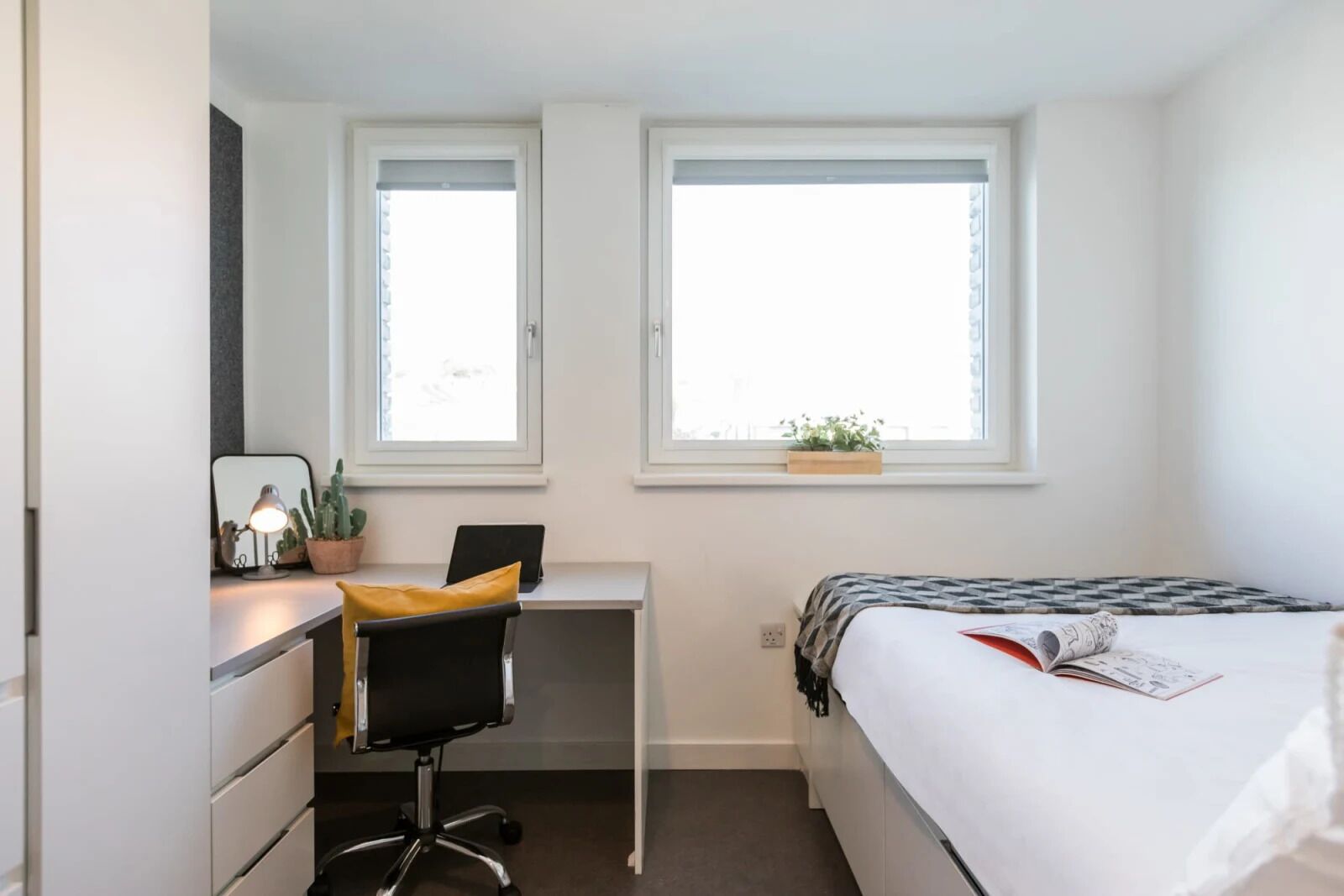 A bedroom with a desk, chair, bed, and windows.