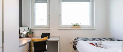 A bedroom with a desk, chair, bed, and windows.